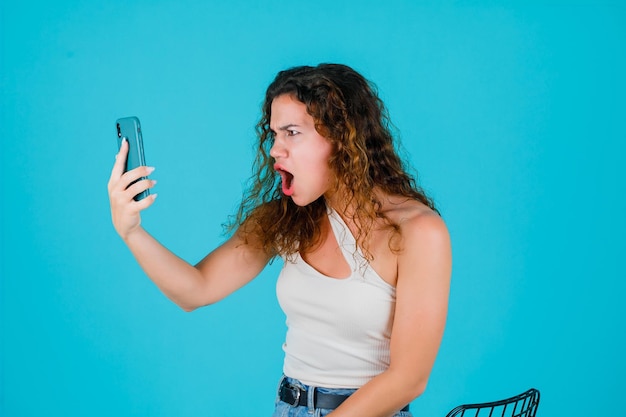 Young girl is talking on video call by screaming on blue background