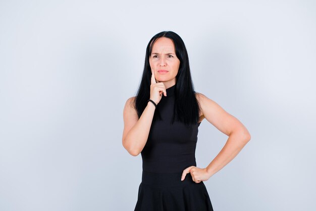 Young girl is thinking by holding forefinger on cheek on white background