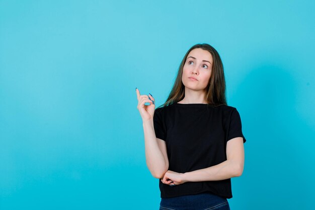 Молодая девушка думает, указывая указательным пальцем на синем фоне
