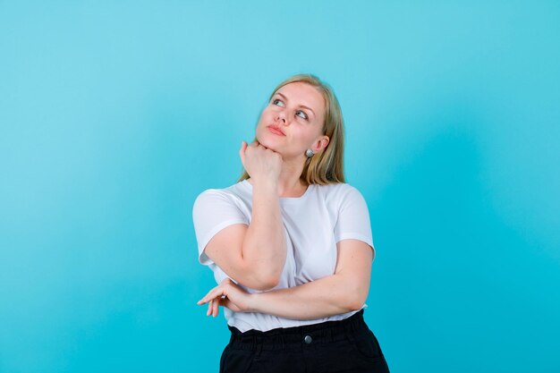 Young girl is thinking by putting fist under chin on blue background
