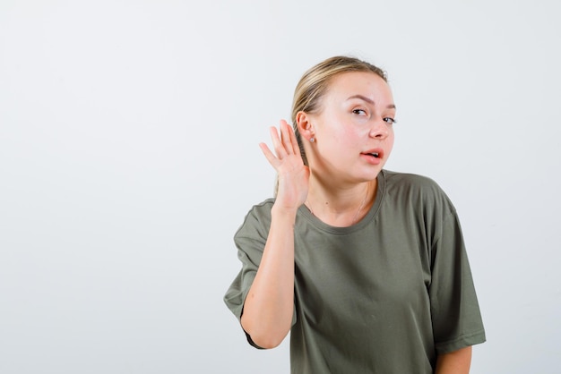 The young girl is trying to listen by holding her hand behind ear on white backkground