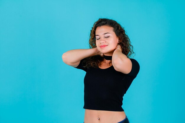 Young girl is wishing by putting hands behind neck on blue background