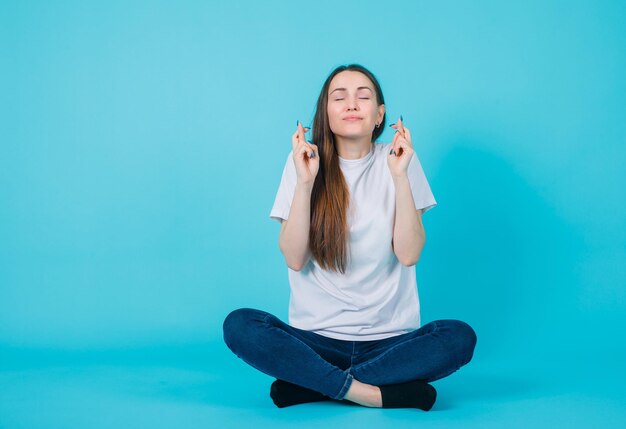 Young girl is wishing by raising up her crossed fingers on blue background