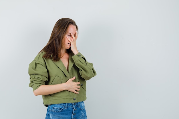 Foto gratuita giovane ragazza in giacca, pantaloncini tenendo la mano sul viso e guardando in difficoltà, vista frontale.