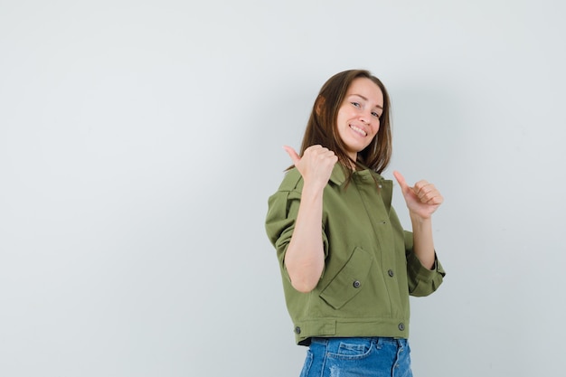 Young girl in jacket, shorts pointing back with thumbs up and looking cheerful .