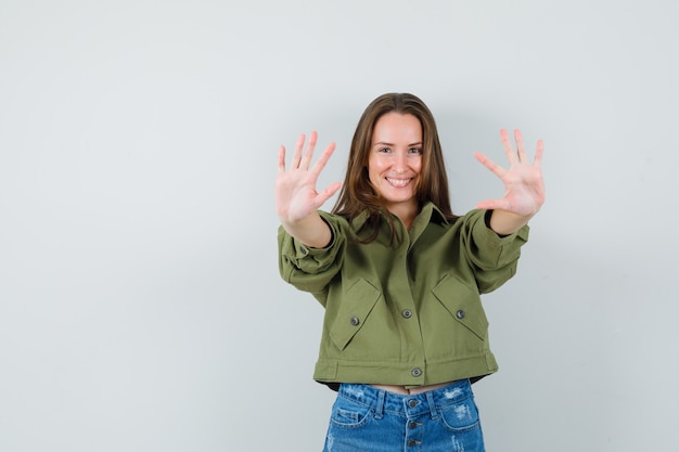 Giovane ragazza in giacca, pantaloncini che mostrano dieci dita e che sembra allegra, vista frontale.