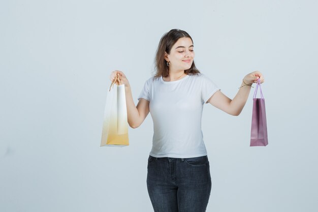 Tシャツ、ジーンズでギフトバッグを保持し、満足そうに見える若い女の子、正面図。