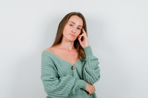 Young girl in knitwear leaning cheek on hand, holding hand under elbow and looking alluring , front view.