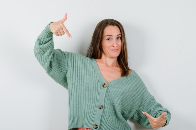 Free photo young girl in knitwear pointing at herself with index fingers and looking confident , front view.