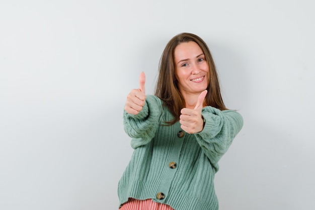 Young girl in knitwear showing double thumbs up and looking happy , front view.