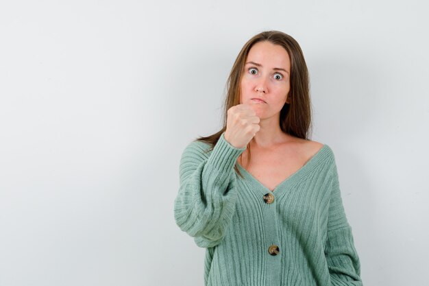 Young girl in knitwear, skirt clenching fist, curving lips and looking serious , front view.