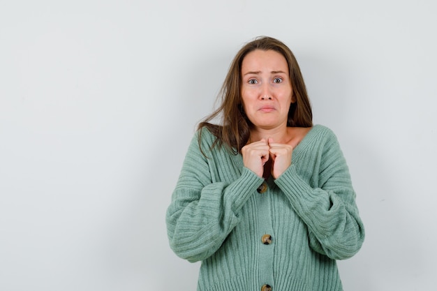 Free photo young girl in knitwear, skirt clenching fists over chest and looking scared , front view.