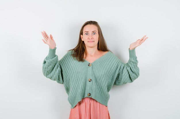 Young girl in knitwear, skirt showing helpless gesture and looking baffled , front view.