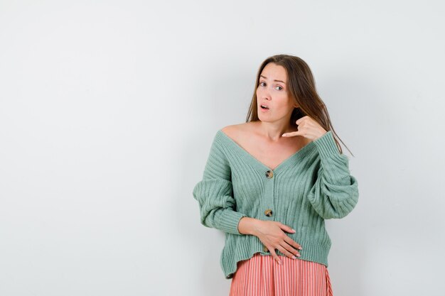 ニットウェアの若い女の子、電話のジェスチャーを示し、魅力的に見えるスカート、正面図。
