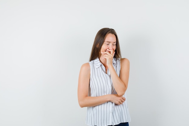 Молодая девушка смеется с рукой над ртом в футболке, вид спереди джинсы.