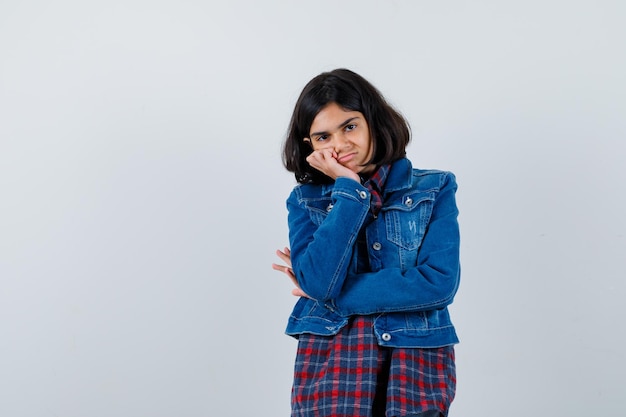 Young girl leaning cheek on palm in checked shirt and jean jacket and looking cute. front view.