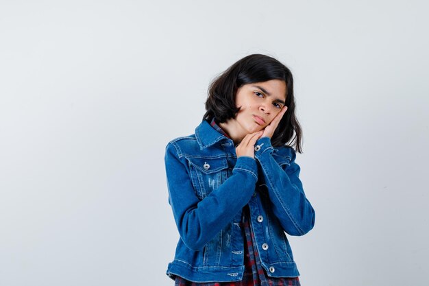 Young girl leaning cheek on palm in checked shirt and jean jacket and looking serious , front view.