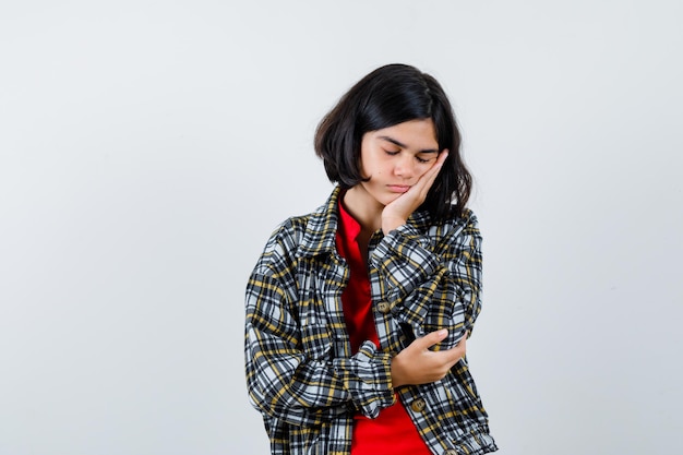 Giovane ragazza appoggiata guancia sul palmo, fingendo di dormire in camicia a quadri e t-shirt rossa e guardando assonnato, vista frontale.