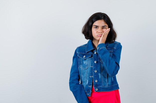 赤いTシャツとジージャンで手のひらに頬をもたれ、疲れているように見える若い女の子