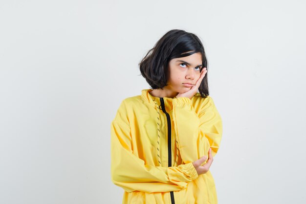 Young girl leaning cheek on palm and thinking about something in yellow bomber jacket and looking pensive.