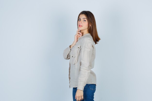Young girl leaning chin on hand in beige shirt, jeans and looking cute , front view.