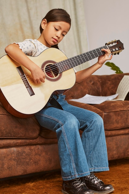 家でギターを弾く方法を学ぶ少女