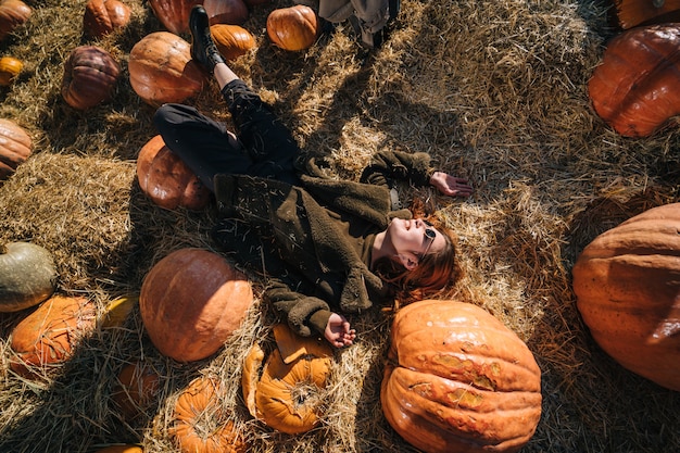 Young girl lie on haystacks among pumpkins. View from above