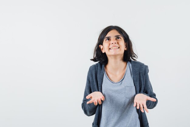 Young girl in light gray t-shirt and dark grey zip-front hoodie stretching hand as trying to hold something and looking above and looking excited