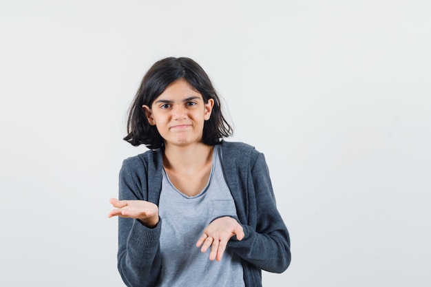 Young girl in light gray t-shirt and dark grey zip-front hoodie stretching hands toward camera and looking cute ,