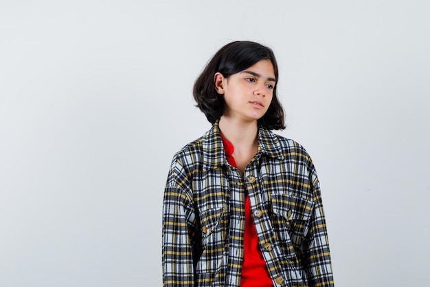 Young girl looking away while posing at camera in checked shirt and red t-shirt and looking serious , front view.