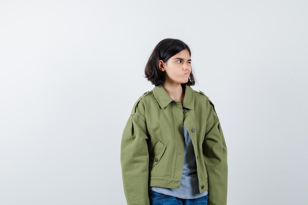 Young girl looking away while posing  in grey sweater, khaki jacket, jean pant and looking serious , front view.