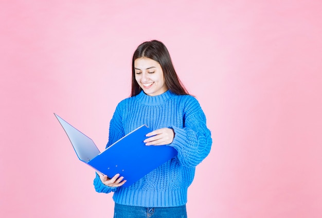 young girl looking at a blue folder on pink.