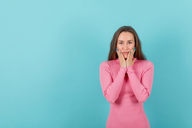 Young girl looking at camera by holding hands on cheeks on blue background