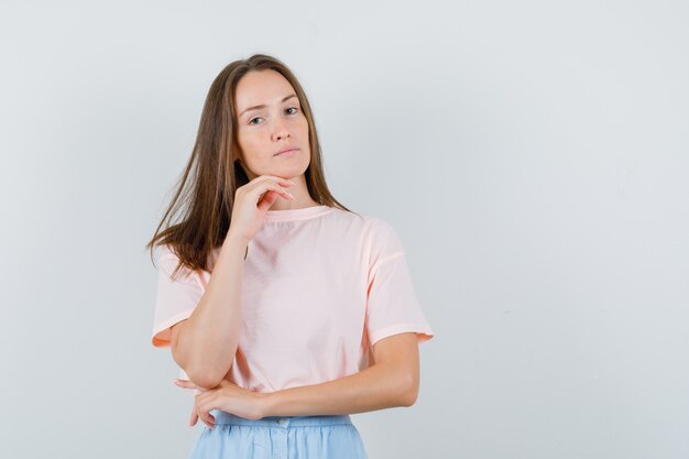 Молодая девушка смотрит в камеру в футболке, юбке и задумчиво, вид спереди.