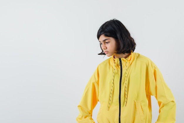 Free photo young girl looking down, posing at camera in yellow bomber jacket and looking serious.