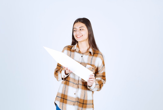 Young girl looking at empty speech arrow pointer on white wall. 