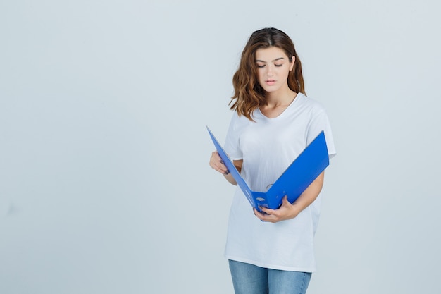Young girl looking into folder in white t-shirt and looking focused. front view.