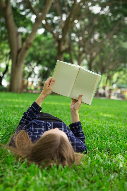 Free photo young girl lying on grass and reading book