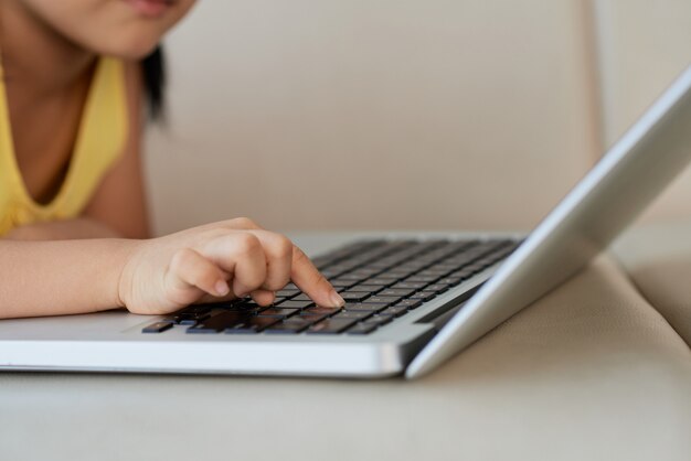 Young girl lying on sofa and pressing button on laptop with one finger