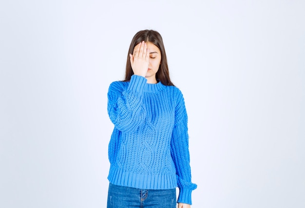 young girl model in blue sweater coning eye with a hand on white-gray.