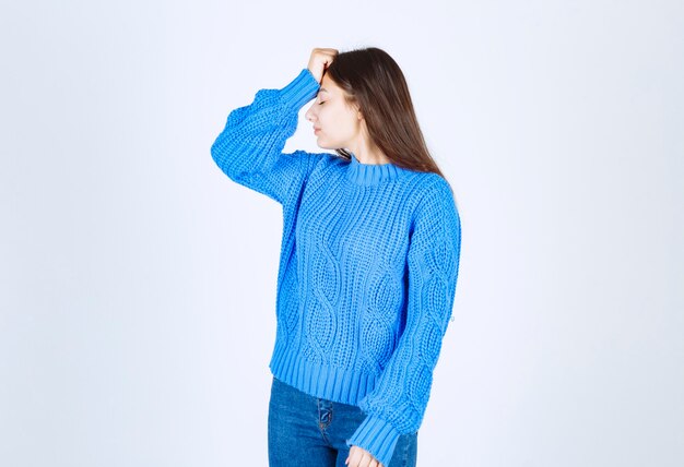 young girl model in blue sweater holding hand near forehead .