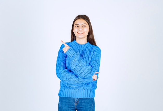 young girl model in blue sweater pointing away on white-gray.
