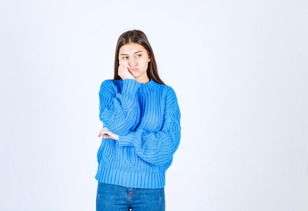 白灰色で立ってポーズをとる青いセーターの若い女の子モデル。