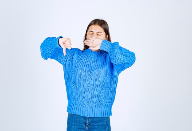 young girl model in blue sweater yawning and showing a thumb down .