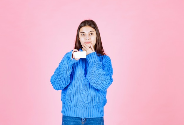 young girl model holding a card on pink wall.