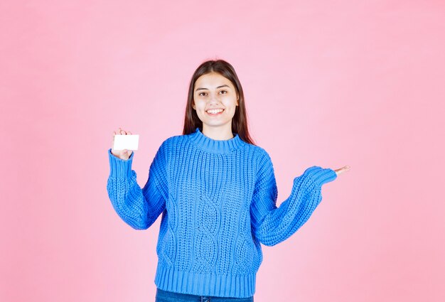young girl model holding a card on pink wall.