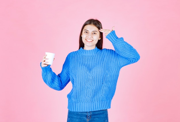 young girl model holding a plastic cup on pink wall.