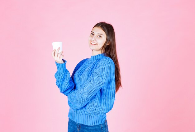 ピンクの壁にプラスチック製のコップを保持している若い女の子モデル。