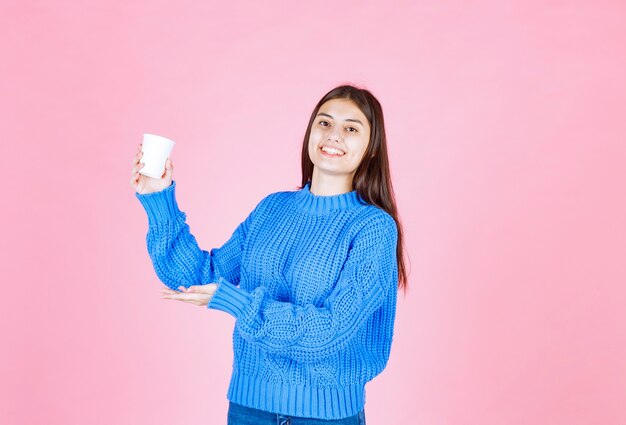 ピンクの壁にプラスチック製のコップを保持している若い女の子モデル。