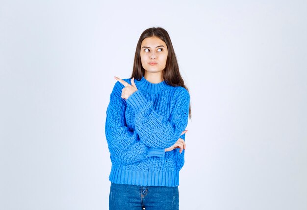 young girl model pointing away on white wall.